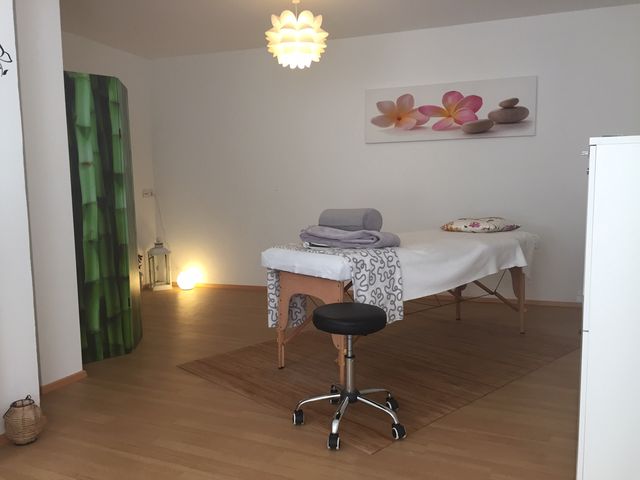 Heller Behandlungsraum mit Behandlungsliege, Kerzenlicht und Blumenbild