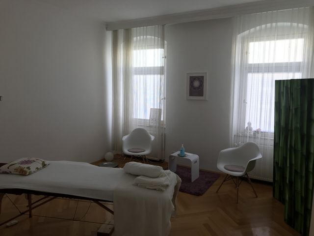 Large bright room with tall windows, a treatment table and two white chairs
