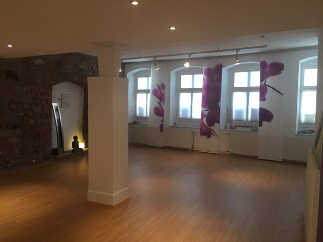 Großer Trainingsraum mit Holzboden, Sandsteinwand und hohen Fenstern